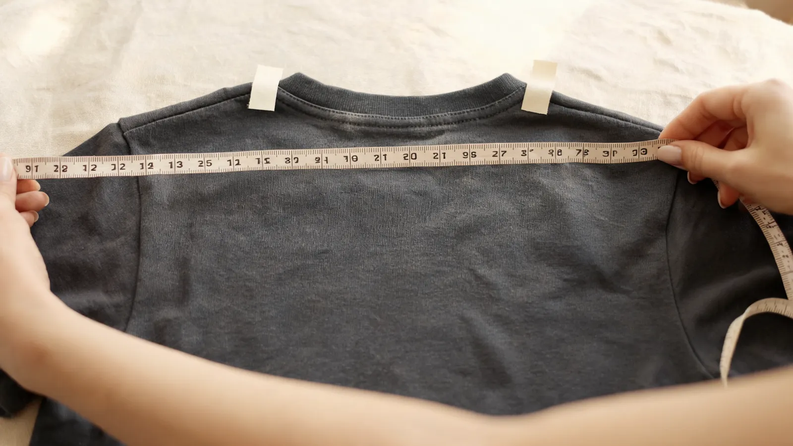 Measuring across the upper back of a flat garment with paper markers at the collar seam